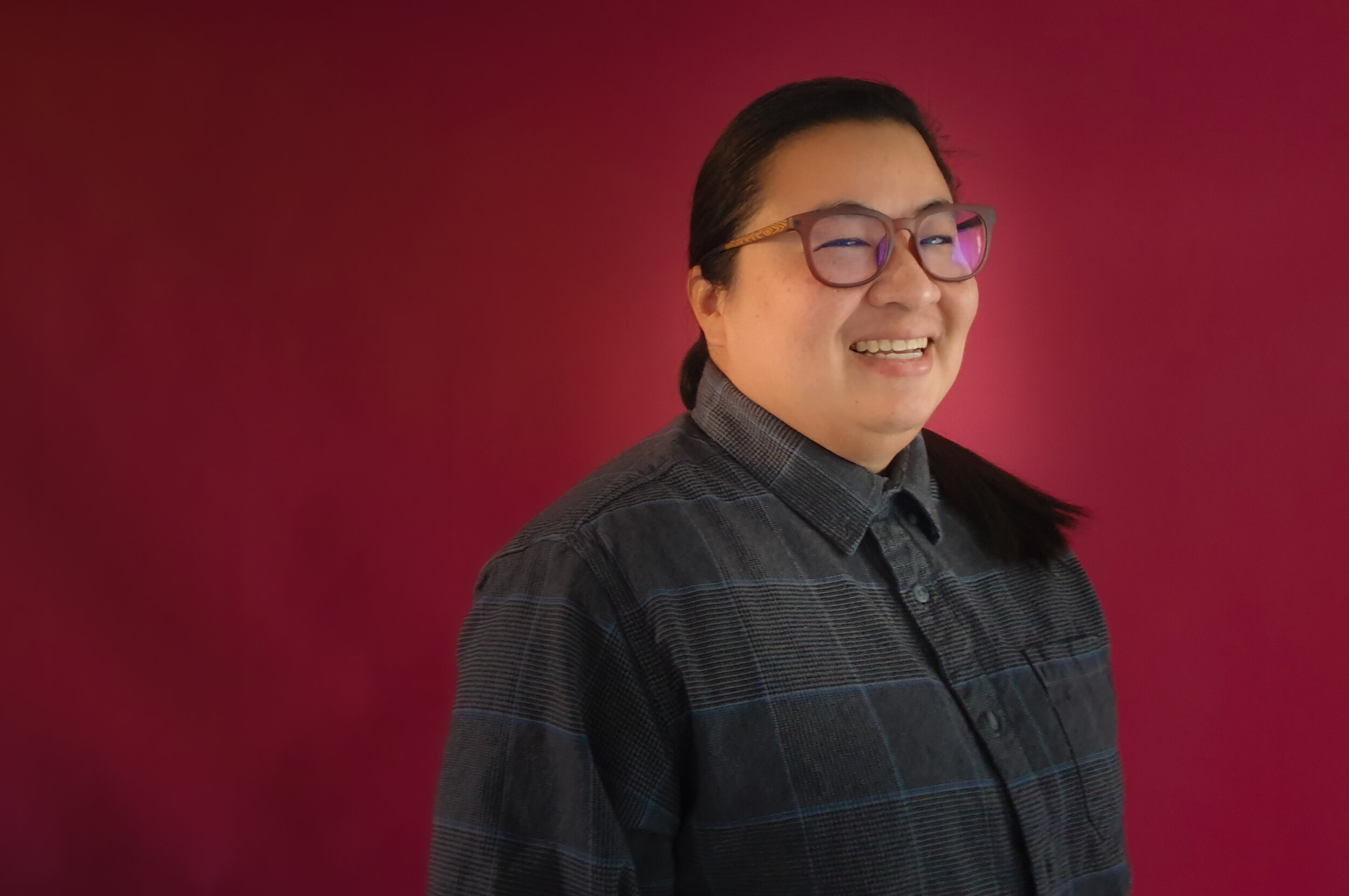 Southeast Asian person wearing glasses smiles at the camera.