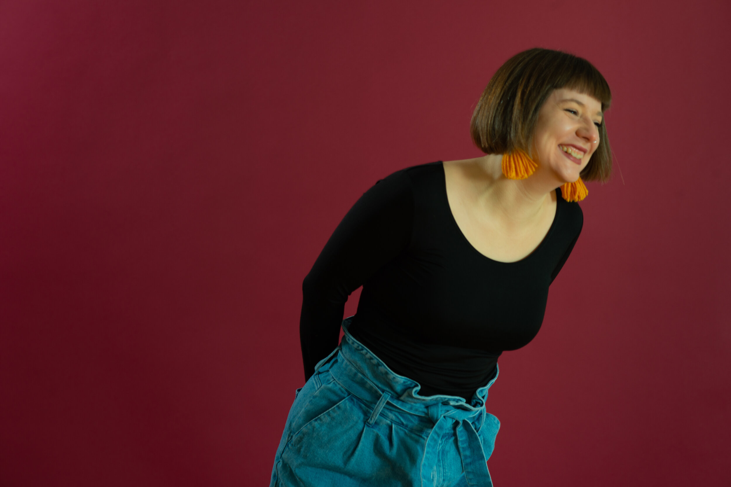 White woman with brown hair and yellow earrings laughs.